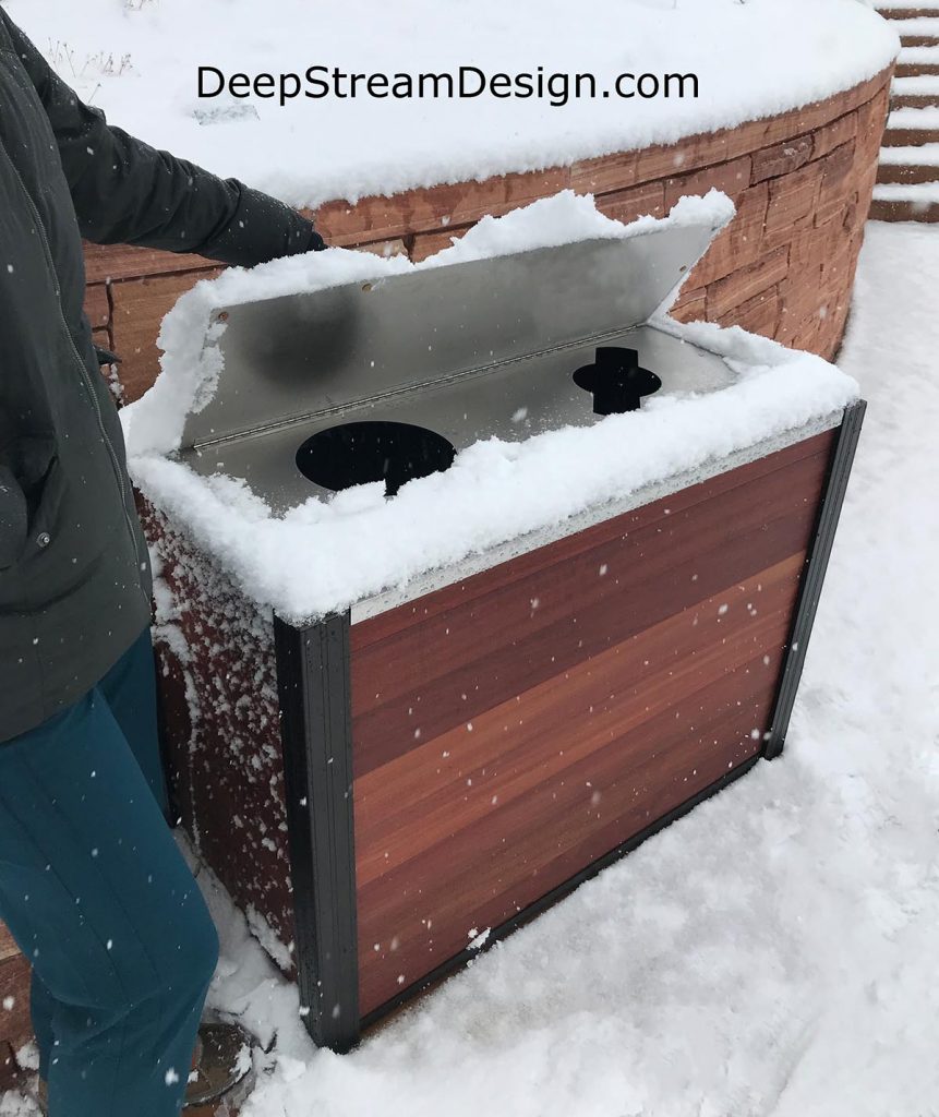 An outdoor modern combination trash bin and recycling receptacle with a weatherproof lid shown with a lot of snow on top and all around